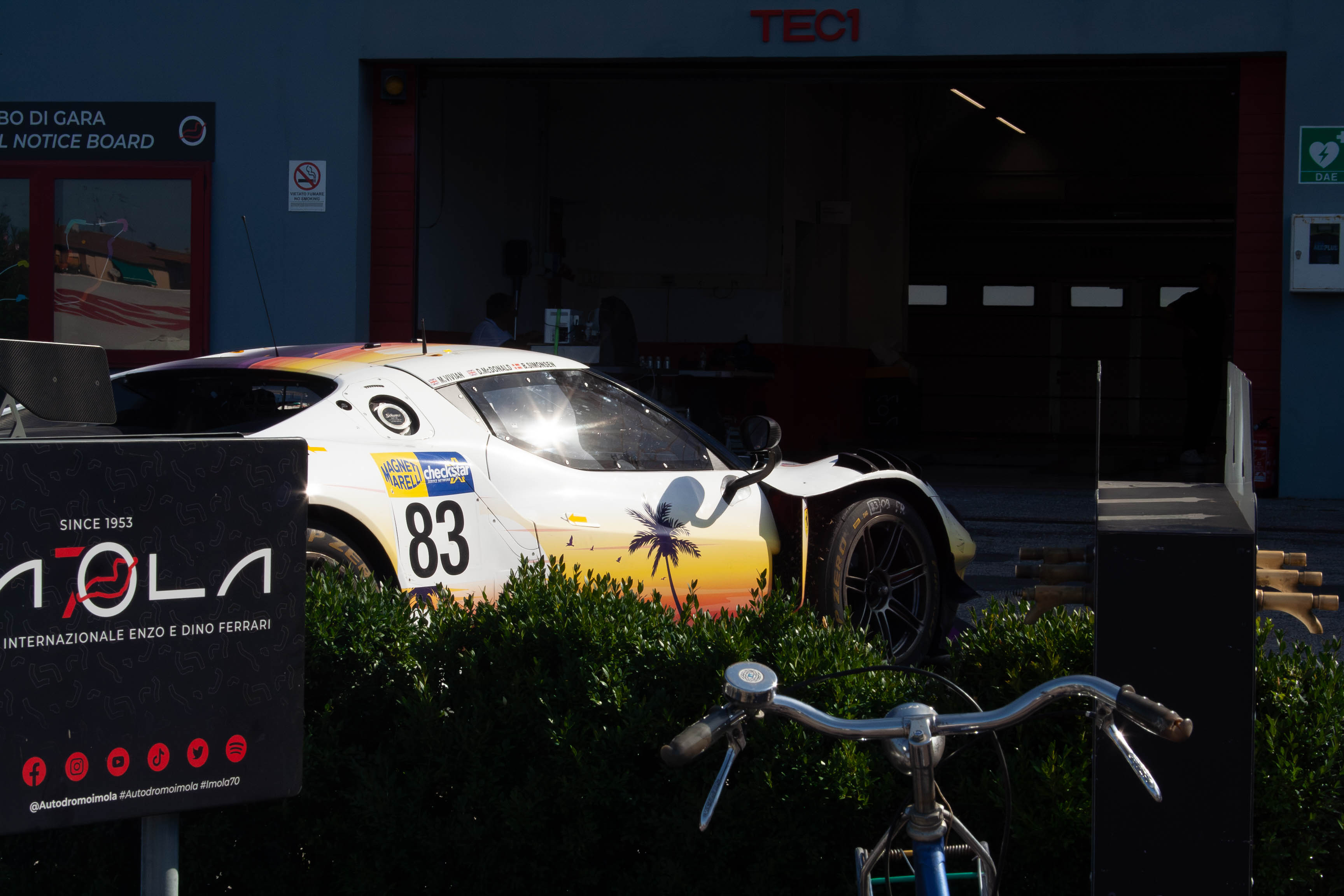 Lamera Cup car #83 parked outside a pit garage with sunset tropical livery at Imola Circuit
