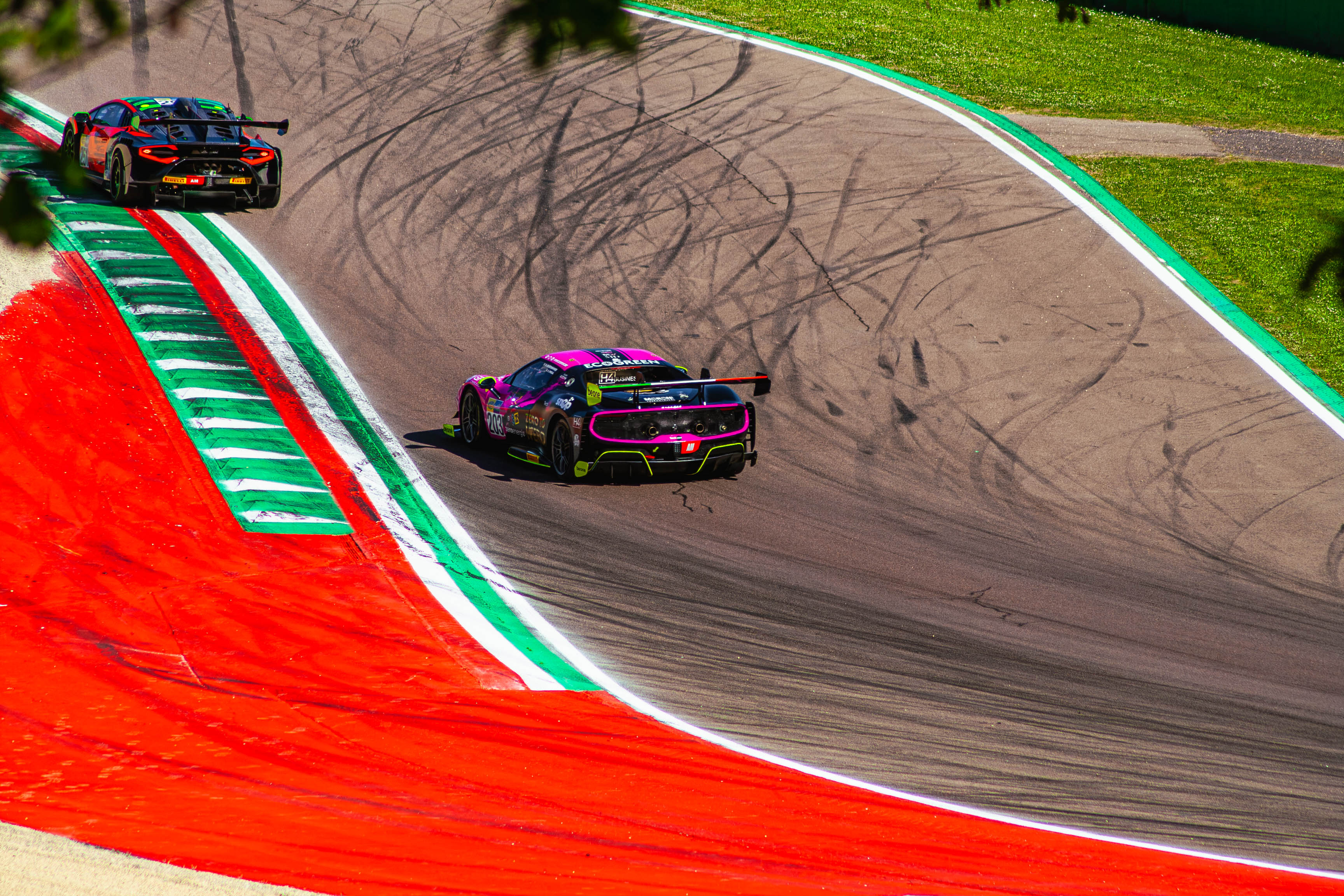 Rear view of Ferrari 296 Challenge race cars cornering over red kerbs at Imola Circuit